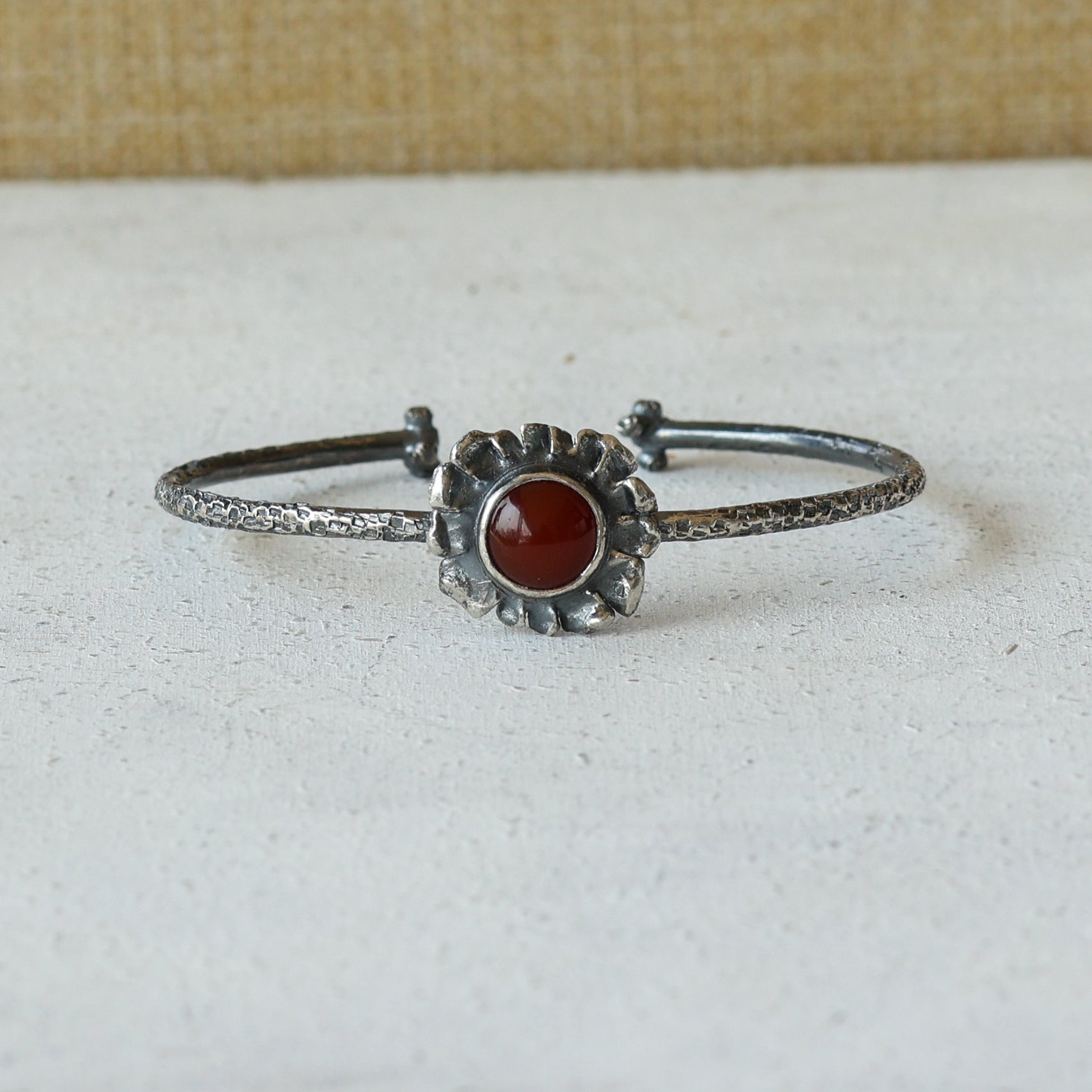 Silver cuff bracelet with a carnelian stone on a white surface