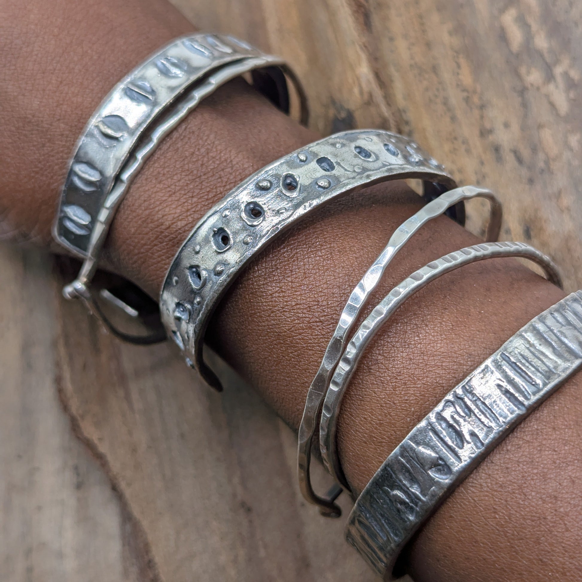 Silver bracelets on a wrist against a wooden background