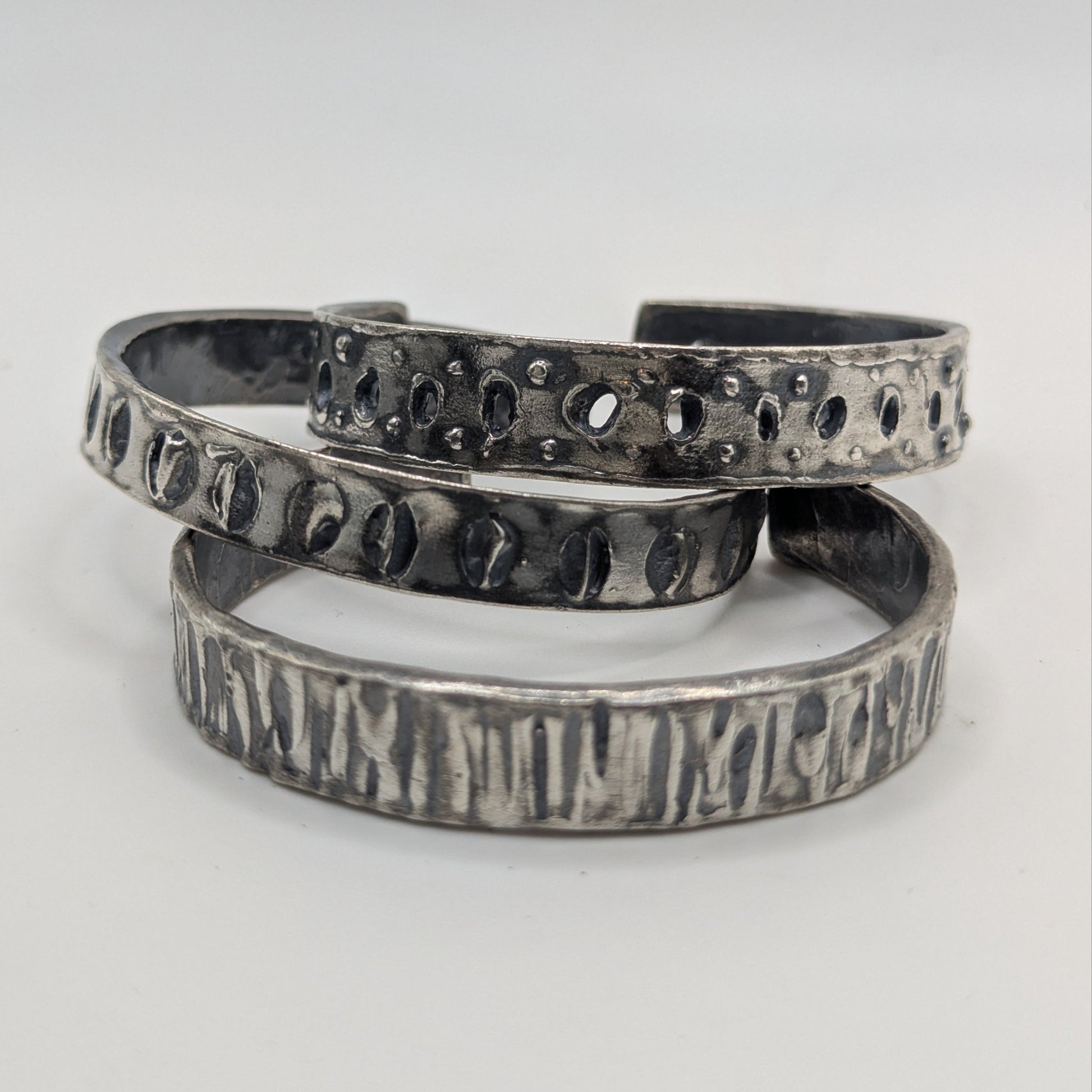 Set of three silver bracelets with textured designs on a white background