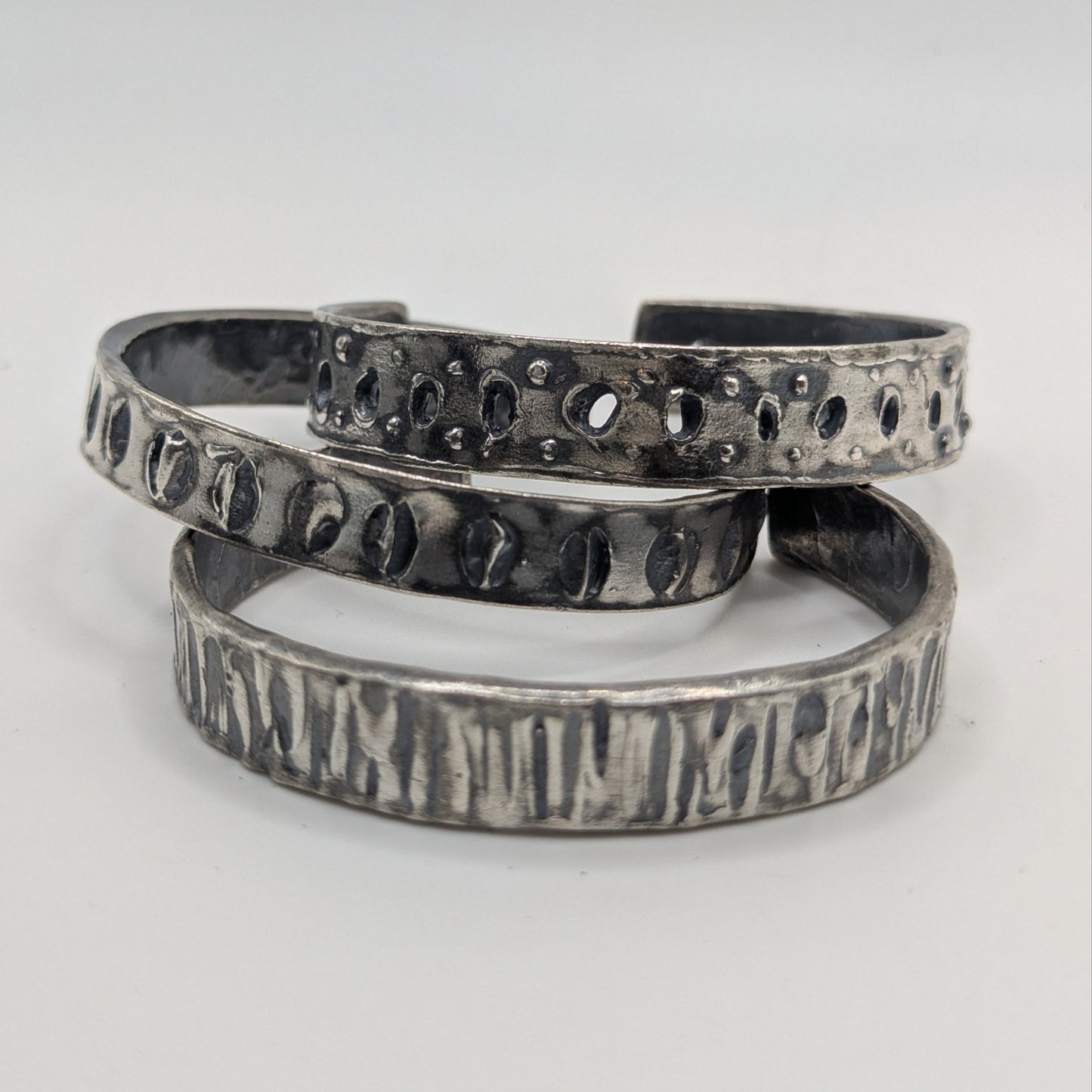 Set of three silver bracelets with textured designs on a white background