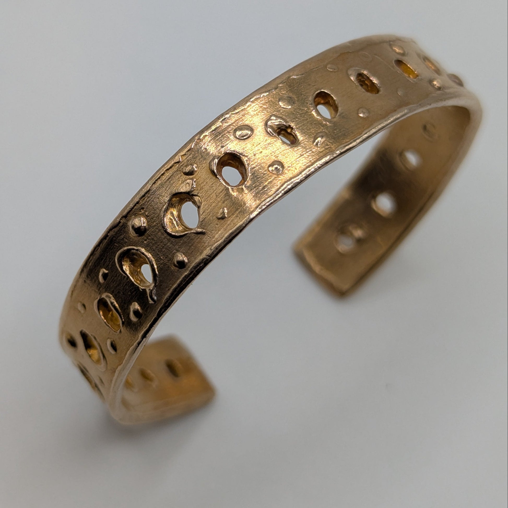 Gold bracelet with intricate patterns on a light gray background
