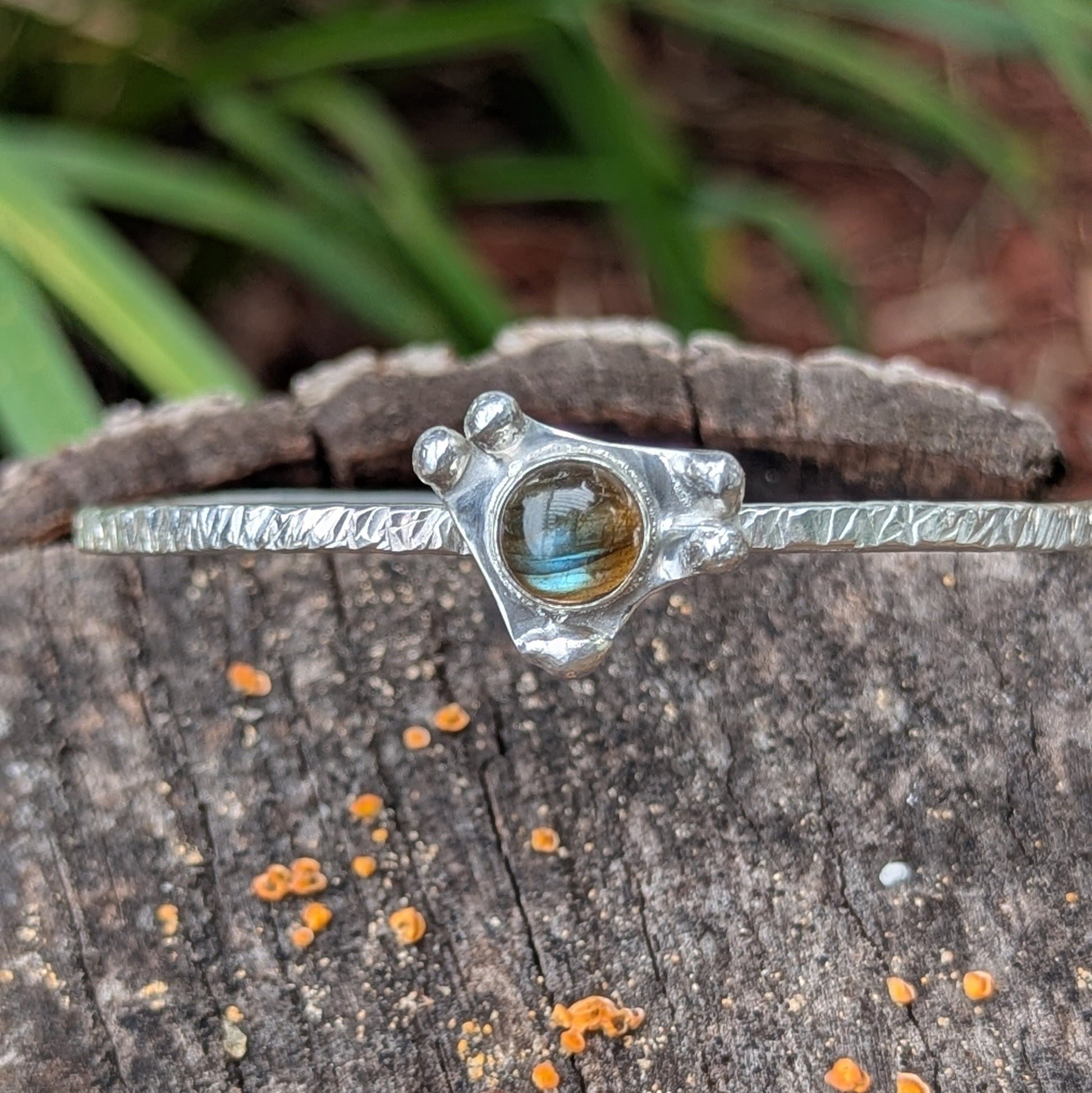 Silver bracelet with a labradorite gemstone on a wooden surface with fungi.