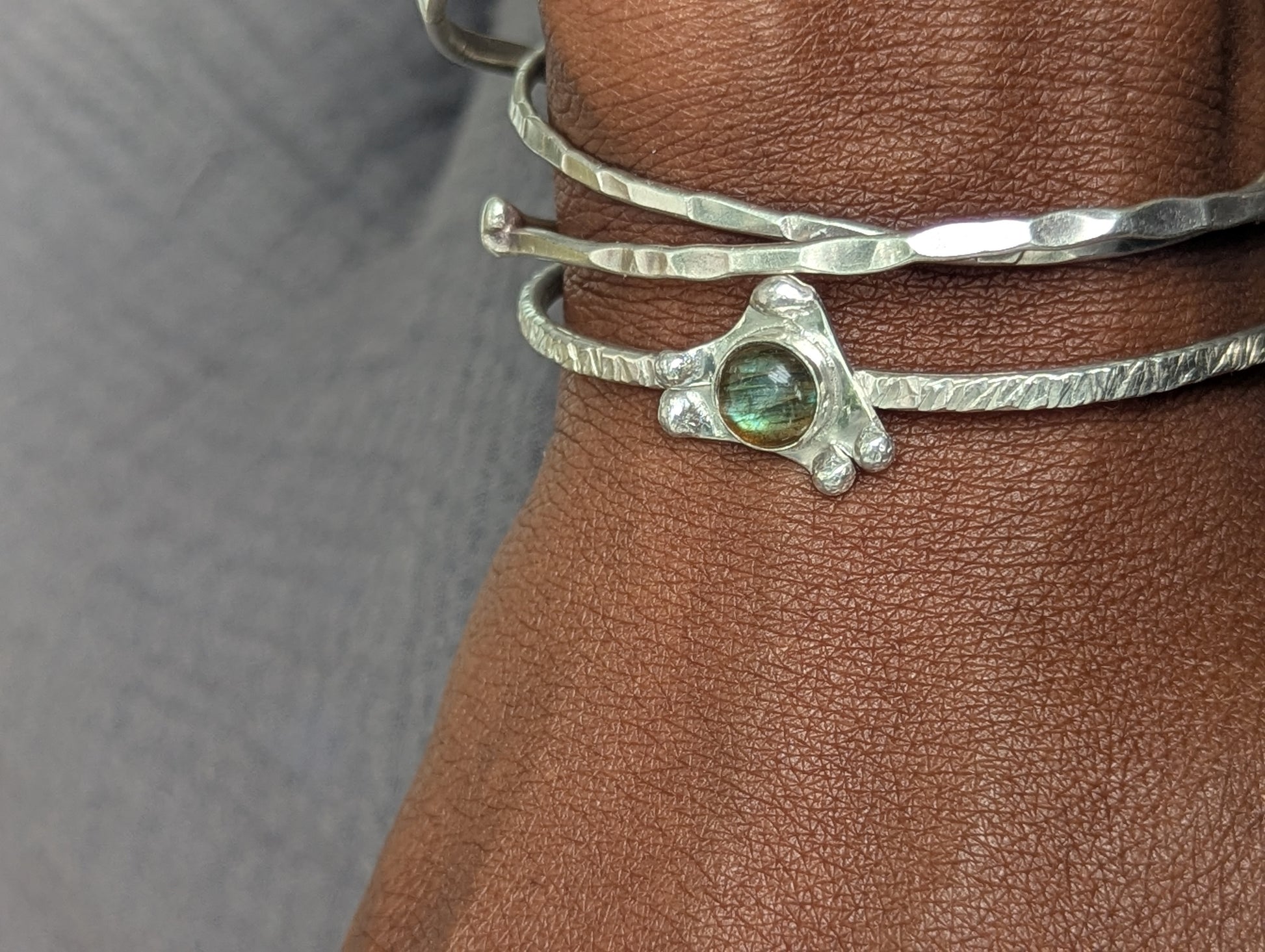 Silver bracelet with a green gemstone on a wrist against a neutral background