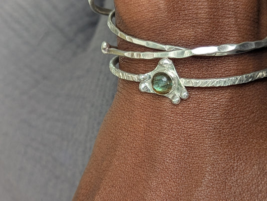 Silver bracelet with a green gemstone on a wrist against a neutral background
