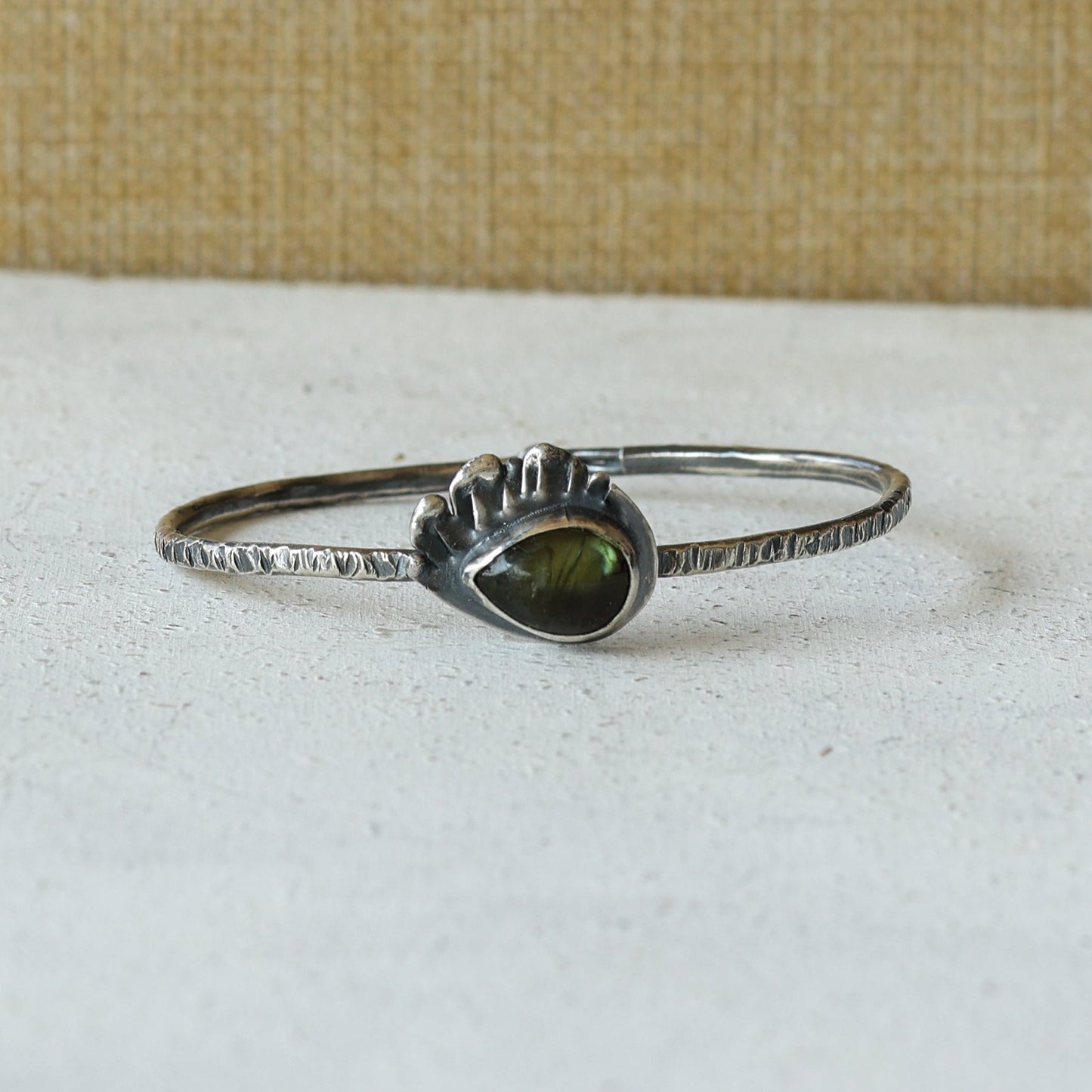 Silver bracelet with a green labradorite gemstone on a white surface