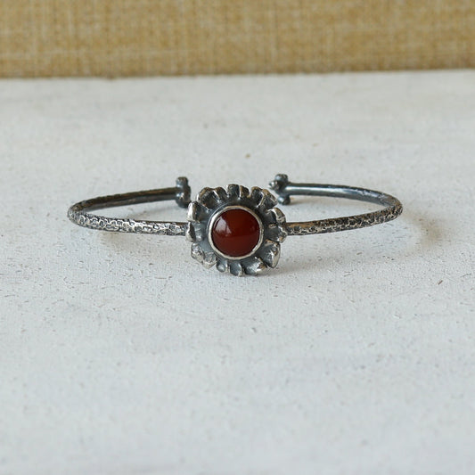 Silver cuff bracelet with a carnelian stone on a white surface